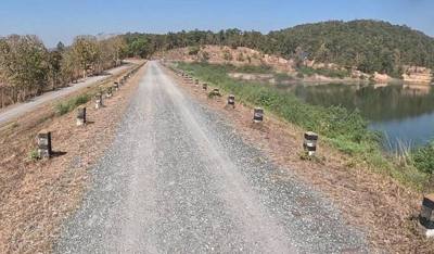 Engineered road on embankment with formal milestone markers, Thailand. Fresh coarse gravel dressing over compacted base.