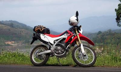 A Honda CRF250L 2013 model with the Mekong river, and Laos beyond, in the background; Road number 1129, in Chiang Rai province, Thailand. The waterproof bag…