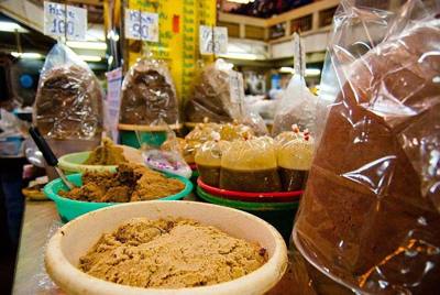 Baskets and mounds of different types of kapi (Thai shrimp paste) and tightly sealed bags of pla raa (a thicker type of fish sauce) at Warorot market in…