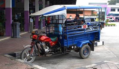 A motorbike with a cab attached to it, similar to a tuk-tuk. The cab features benches on both sides, much like a songthaew. The photo was made at the new bus…