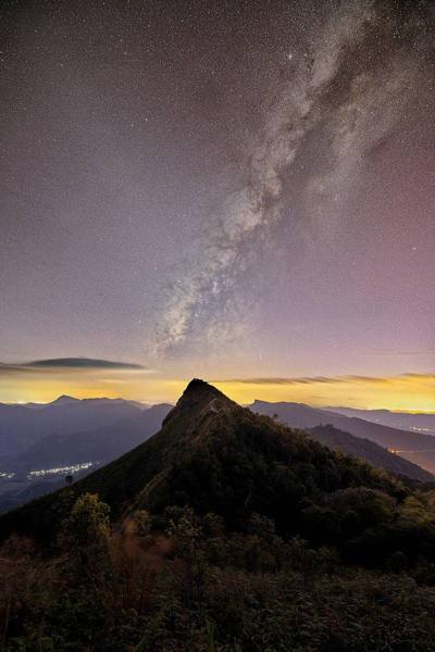 A spectacular time-blending photograph capturing the Milky Way galaxy stretching across the pristine night sky over the iconic peak of Phu Chi Fa, located…