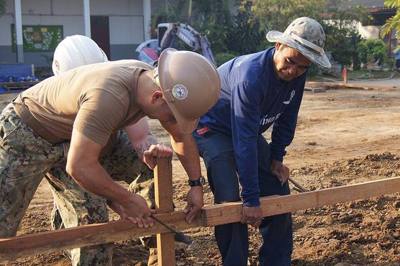 Chief Steelworker Mike Bonifer, center, and Builder 1st Class Moses Silva, left, assigned to Naval Mobile Construction Battalion 5, work together with the…