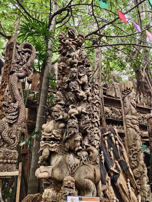 A tower of carved figures under the trees at Ban Tipmanee