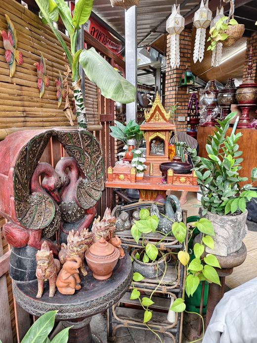 A spirit house among potted plants and terracotta figures at Non's Khao Soi