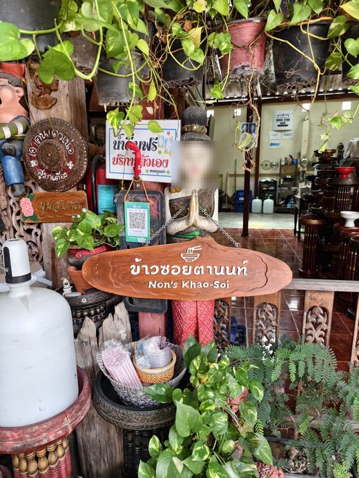 Non's Khao Soi under hanging plants: carved figures, a free drinking-water sign