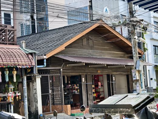 An old teak shophouse with a tin roof among newer buildings