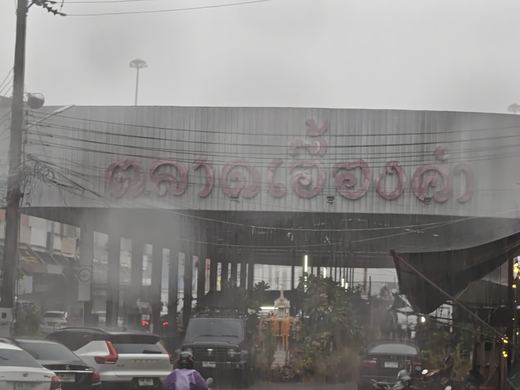 Aueng Kam Market's roof sign in the rain, a spirit house at the gate