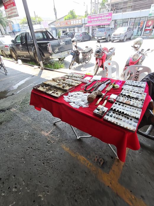 An amulet table under the trees by the car park, phone shops across the road