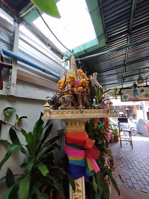 The Garden's spirit house in the alley, marigolds and a rainbow sash