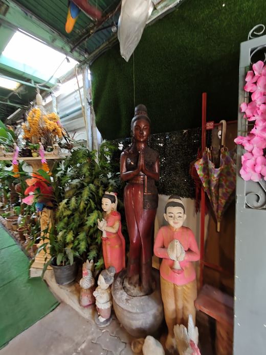 Statues at the Garden: a tall wooden figure and two children in pink, hands together in a wai