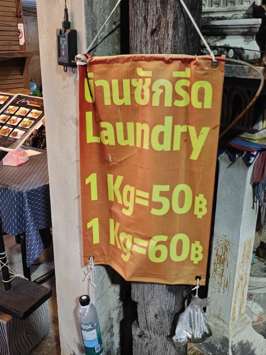 A laundry sign tied to a post: 1 kg 50 baht, 1 kg 60 baht