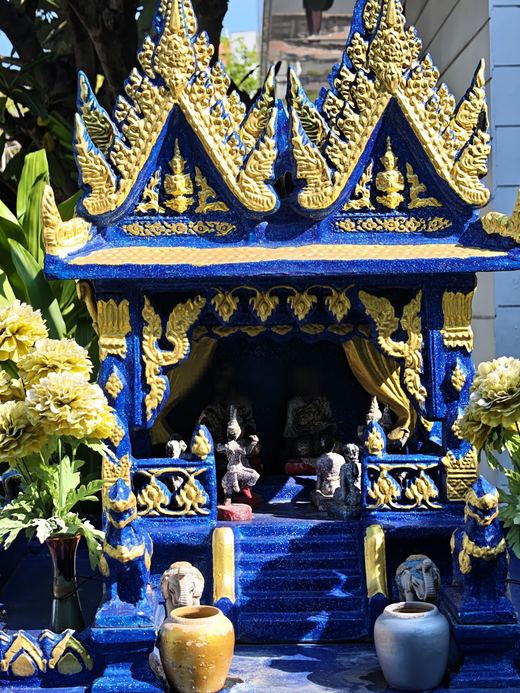 A blue-and-gold spirit house with yellow flowers