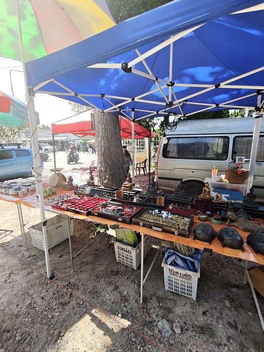 A stall under a blue awning: amulet trays, cases and antiques laid out on red cloth