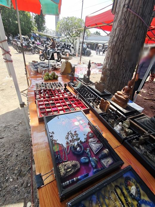 Amulet trays, framed pieces and Buddha images along a stall under a big tree