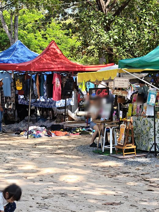 Clothes stalls under red, blue and green awnings in the shade of the trees