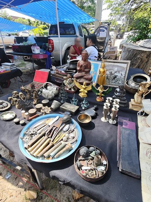 An antiques table: brass Buddha images, a seated monk figure, silver bowls and a tray of old cutlery