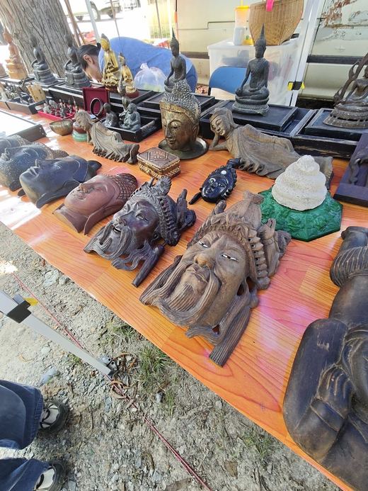 Carved crowned heads, a Buddha head and a white spiral shell along an antiques table