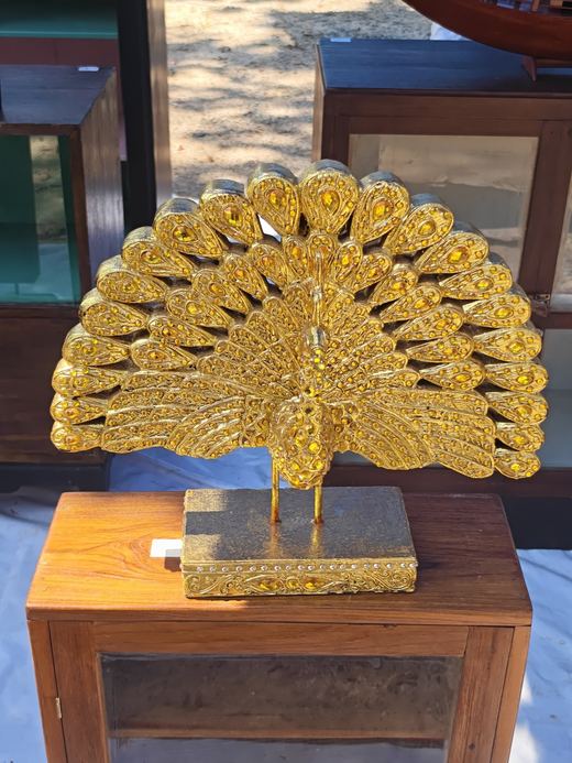 A gilded peacock with its tail fanned, on a teak cabinet