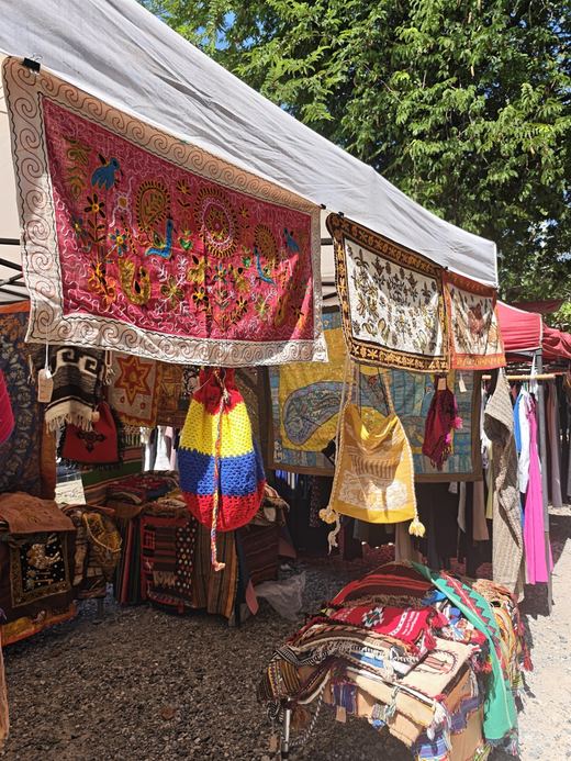 A textile stall: embroidered hangings, woven bags and a bright striped pouch