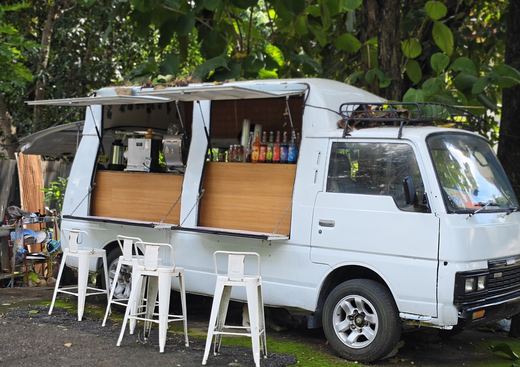 A white coffee van opened up under the trees, steel stools set out