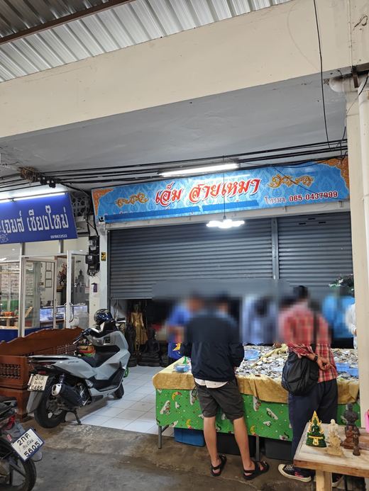 Em Saimao's stall: buyers bent over a glass case of amulets