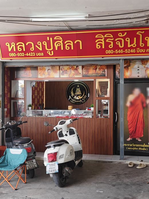 Luang Pu Sila Sirichantho's amulet shop: a red-and-gold sign, the monk's portraits over the counter