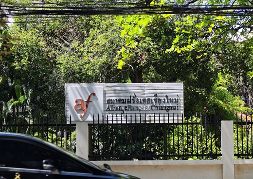 Alliance Française de Chiang Mai's sign over its fence, trees behind