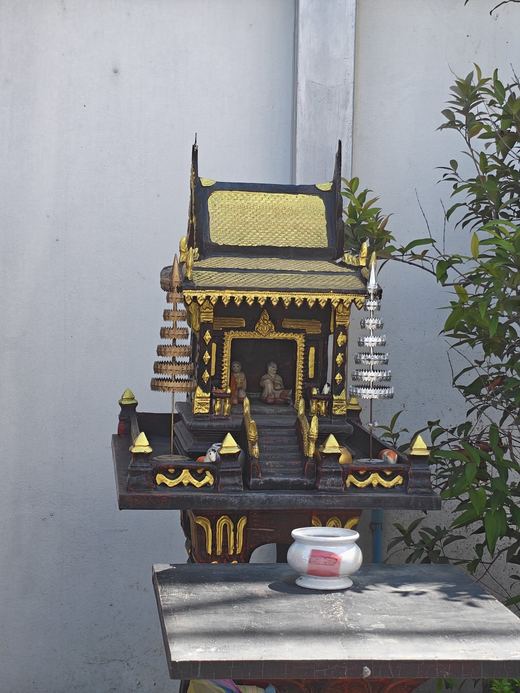 A smaller spirit house with a tiered roof and an incense pot
