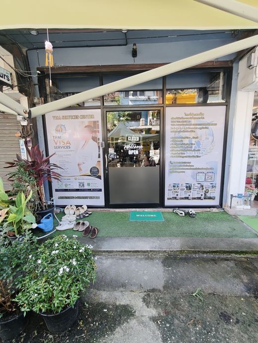 The Thai Visa Services shopfront: posters either side of a glass door, plants on the step