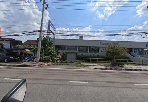 The low grey Carpets Inter showroom with a spirit house at the gate, beside a yard of parked cars and motorbikes.