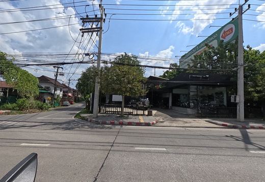 A black-fronted motorbike showroom on a corner with a side lane, under a big green billboard for a housing estate 1 km away.