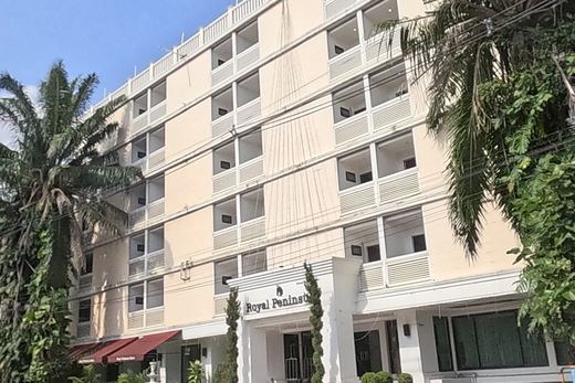 The 'Royal Peninsula' hotel: a six-storey cream building with balconies, palm trees at its entrance, and a small white spirit house with a gilded figure on a pe