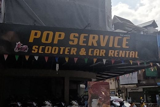 A scooter and car rental shop with a fleet of parked scooters sits beside a dental clinic and a cannabis-dispensary-and-tattoo shopfront.