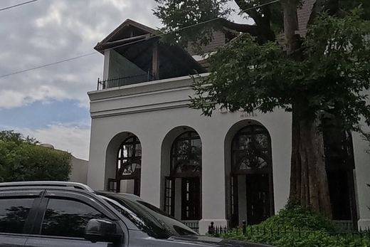 A white colonial-style hotel building with arched windows under a big tree, a beauty accessory shop next door.