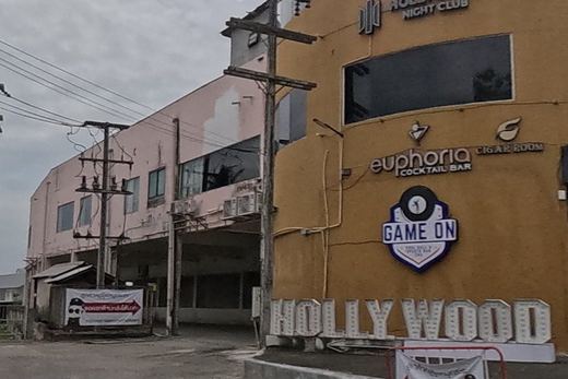 A graffiti-covered remnant of the old city wall with a 'do not walk on ancient wall' sign, facing a yellow nightclub complex lettered 'HOLLYWOOD'.