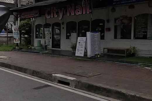 A ground-floor row holds a nail salon with a price board, a cafe with a yellow-striped awning and a soft-serve sign, and a hotel with a red banner.