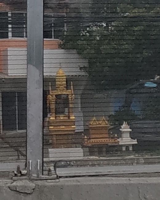 A gold spirit house and a red-and-gold house shrine with a small white stupa, in a yard beside a pickup truck.