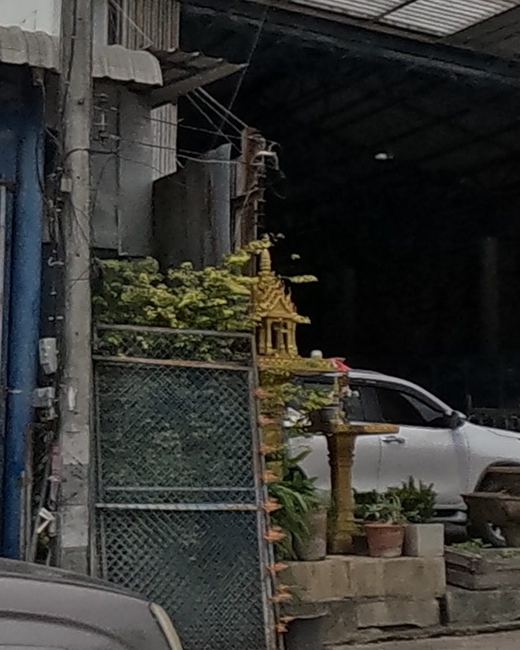 A small gold spirit house by a building-materials yard