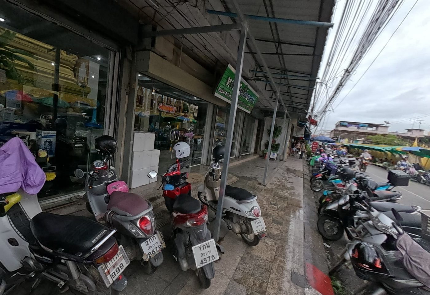 Arcade of shops with parked motorbikes, the street market beyond