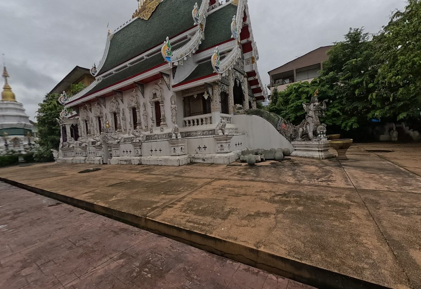 White stucco viharn with green tiered roof, naga stair and a chedi