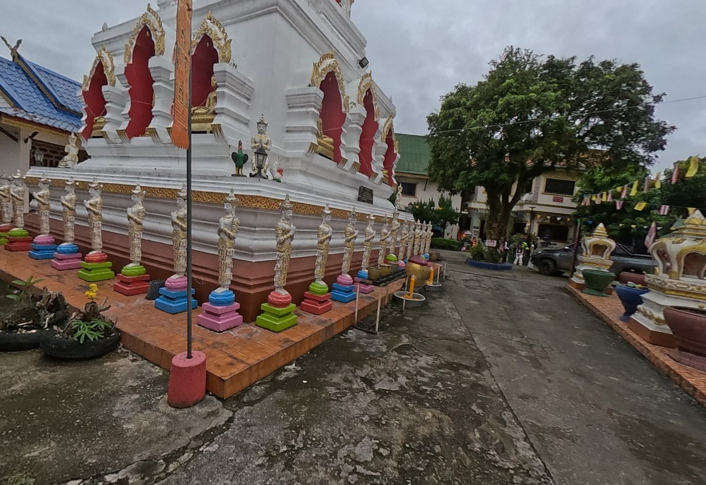 White chedi ringed by standing deva figures on coloured pedestals