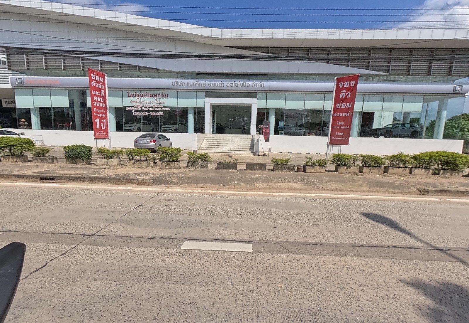The glass front of the Honda showroom with its company name on the fascia and two red banners on poles.