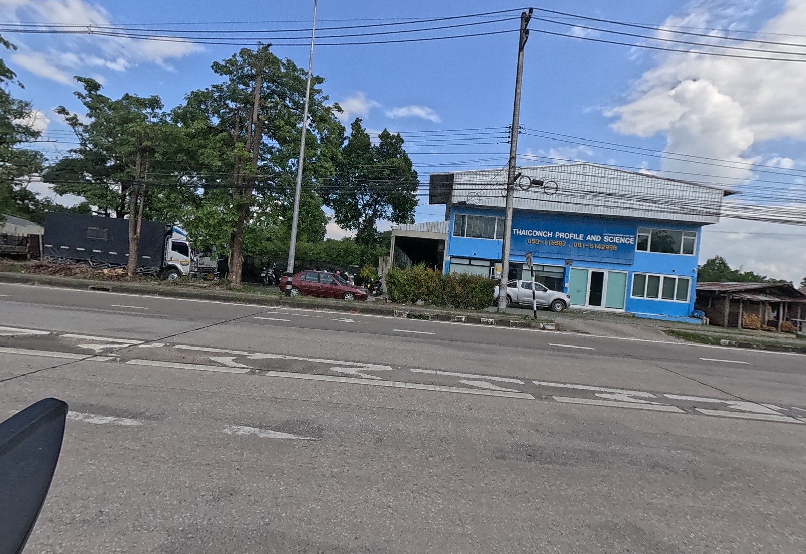 A blue two-storey building signed THAICONCH PROFILE AND SCIENCE with phone numbers, a parked truck and a timber shed beside it.