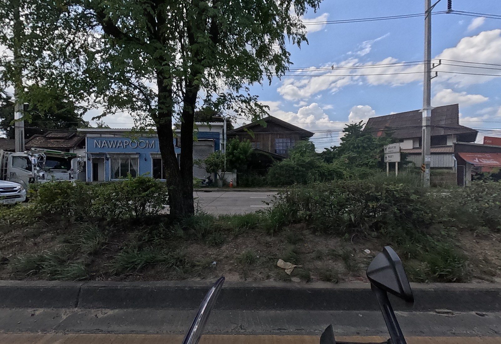 Across the median, a blue building signed NAWAPOOM beside a wooden house, a tow truck and white direction signs.