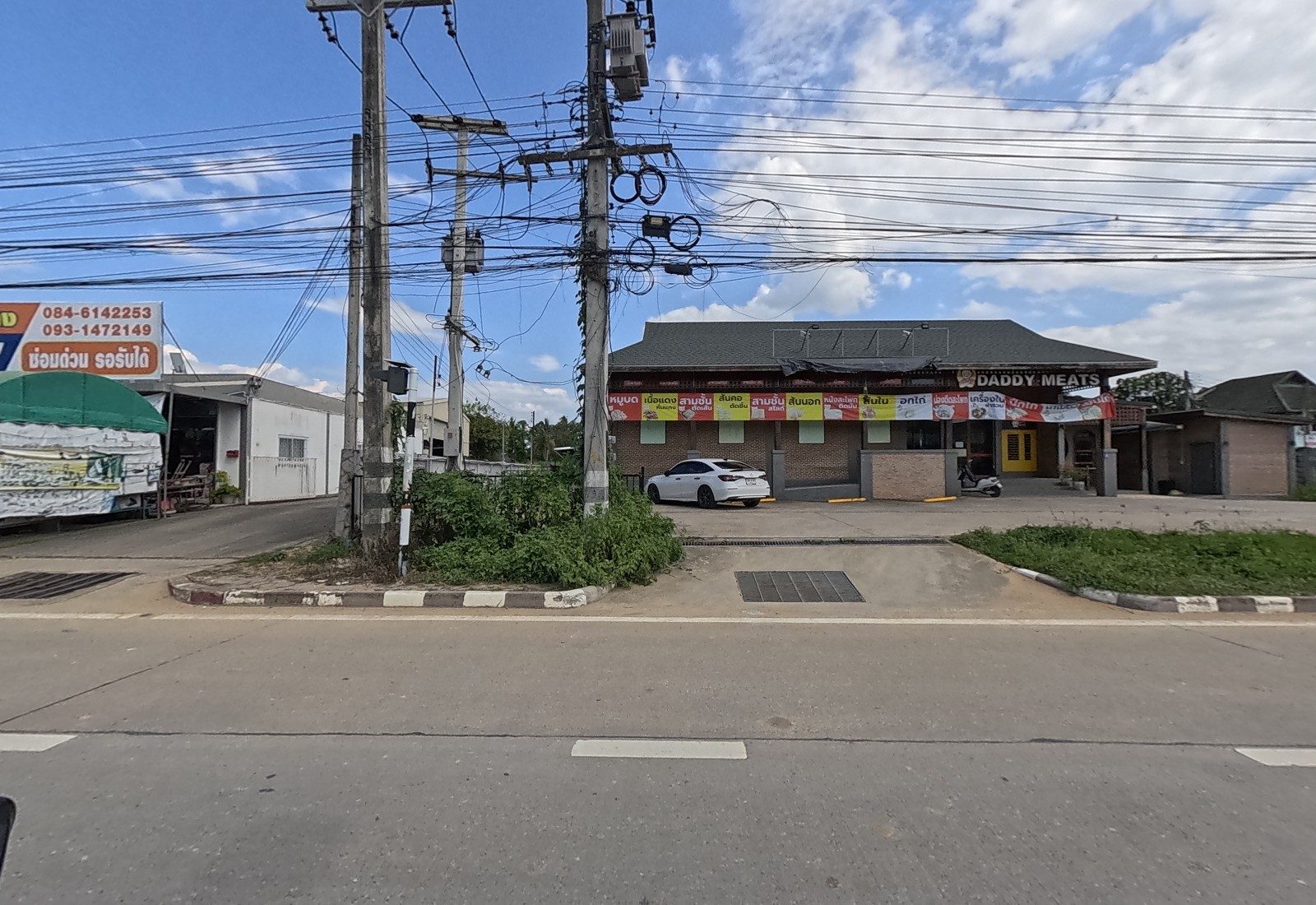 A brick building signed DADDY MEATS with a row of cut-of-meat banners and a parked white car, beside a repair shop sign on the left.