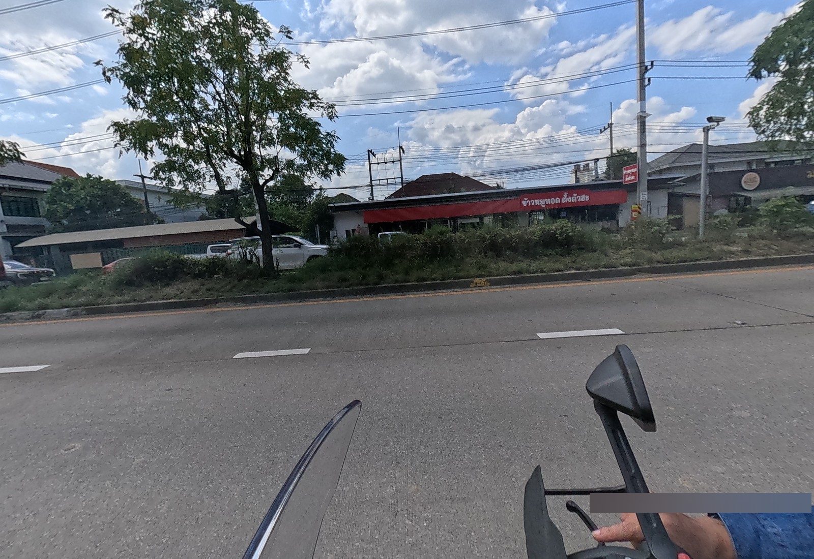 Across the median, the red-fronted ข้าวหมูทอด ตั้งตัวฮะ with a red standing sign, next to the มาลี noodle shop.