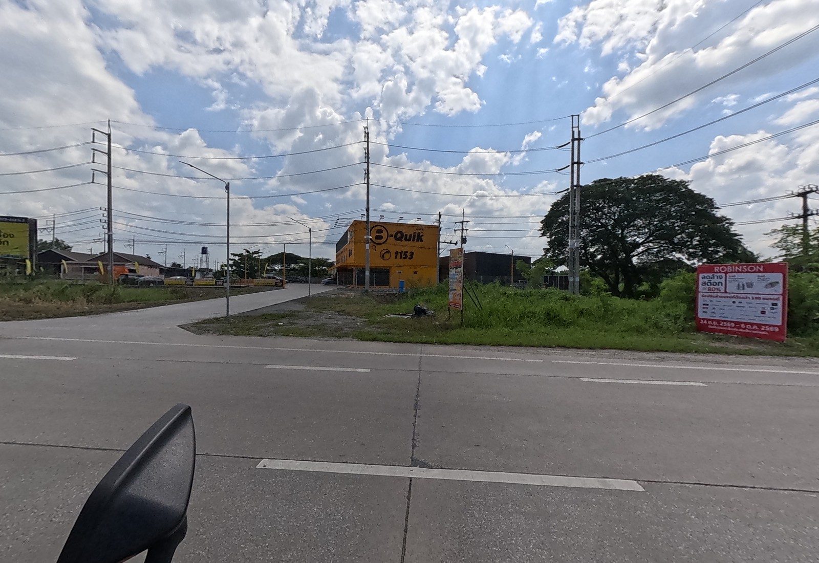 The B-Quik branch with its 1153 sign stands beside a side road; a red Robinson sale billboard stands in the grass.