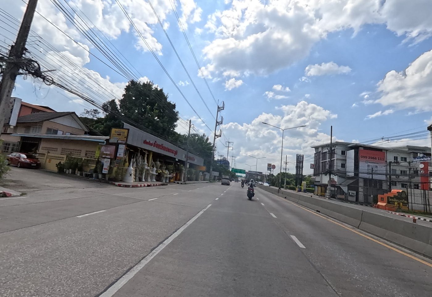 Roadside shop selling spirit houses and white shrines, looking up a highway lined with shops