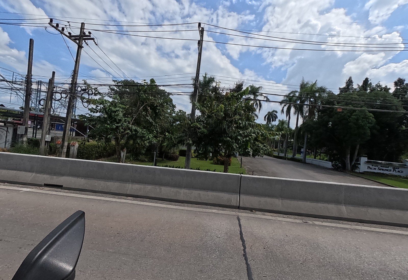The palm-lined entrance drive of PALM SPRINGS PLACE beyond the barrier and a garden.
