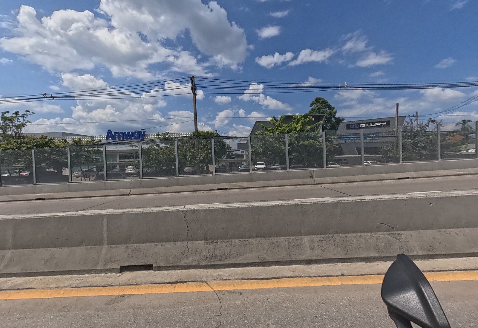 Across the flyover, the Amway building with its blue sign and the RIWAY building behind a car park and trees.